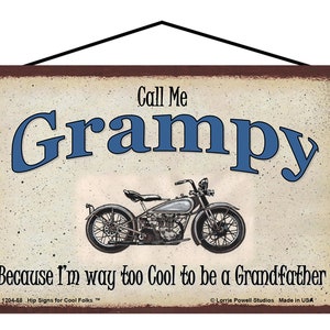 May include: A vintage-style metal sign with a brown background and white text. The sign features a motorcycle and the text "Call Me Grampy Because I'm way too Cool to be a Grandfather".
