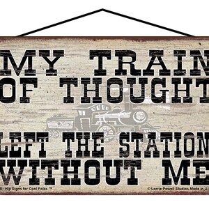 May include: Wooden sign with the text "MY TRAIN OF THOUGHT LEFT THE STATION WITHOUT ME" in black block letters. A faded image of a train is in the center. The sign has a distressed, vintage look.