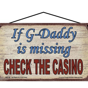 Peut inclure: Une pancarte en bois rustique avec une finition vieillie. La pancarte a un texte bleu et blanc qui dit "If G-Daddy is missing CHECK THE CASINO". La pancarte a une bordure brune et un petit texte en bas qui dit "Hip Signs for Cool Folks".