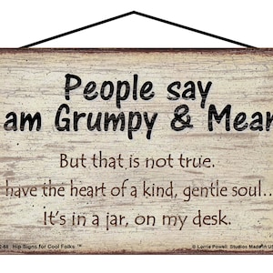 May include: A rustic wooden sign with a white background and brown text. The sign reads "People say I am Grumpy & Mean. But that is not true. I have the heart of a kind, gentle soul... It's in a jar, on my desk."