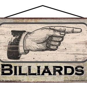 May include: A rectangular wooden sign with a distressed finish, featuring a hand pointing right and the word "BILLIARDS" in bold black letters. The sign includes the text "741R-58 Hip Signs for Cool Folks™" and "Lorrie Powell Studios Made in USA".