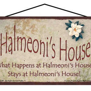 May include: A rustic brown and beige sign with the text "Halmeoni's House" in red. The sign also includes the text "What Happens at Halmeoni's House, Stays at Halmeoni's House!" in red. A white magnolia flower with green leaves is in the upper right corner of the sign.