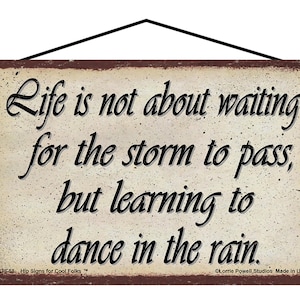 May include: A rustic brown metal sign with a cream background and black text. The sign reads "Life is not about waiting for the storm to pass, but learning to dance in the rain."  The sign is hanging from a black wire.