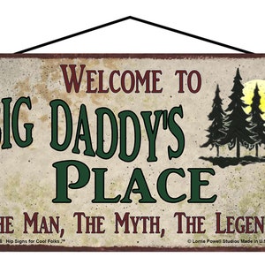 May include: A rustic metal sign with a distressed, aged look. It reads "Welcome to Big Daddy's Place The Man, The Myth, The Legend." The sign features a silhouette of two pine trees and a moon in the background.