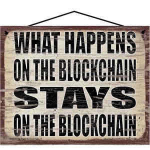 K&ouml;nnte beinhalten: Ein rustikales Holzschild mit einem abgenutzten wei&szlig;en Hintergrund und schwarzem Text, der "What Happens On The Blockchain Stays On The Blockchain" lautet.