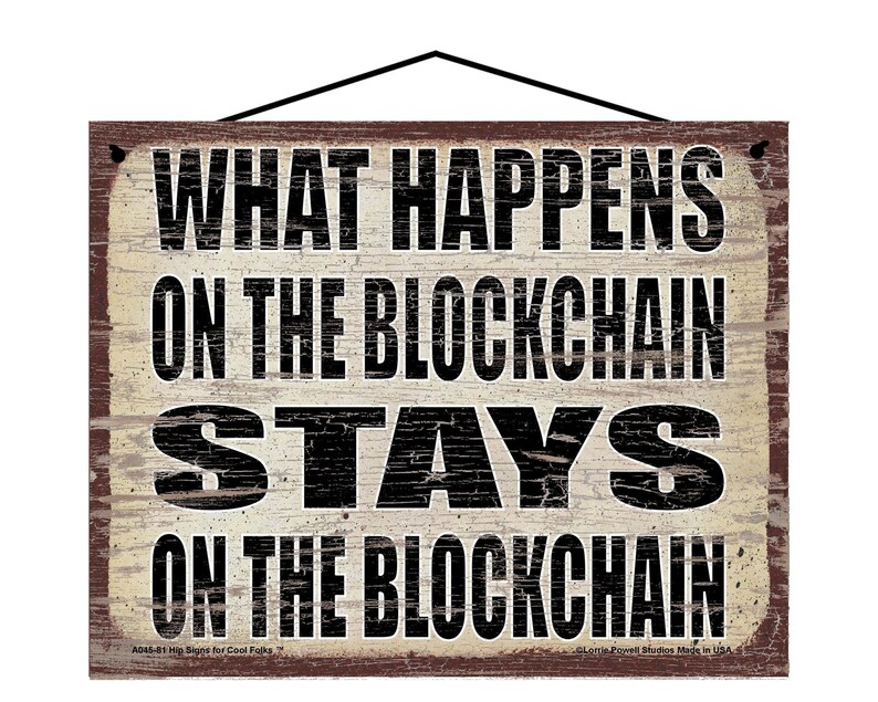 K&ouml;nnte beinhalten: Ein rustikales Holzschild mit einem abgenutzten wei&szlig;en Hintergrund und schwarzem Text, der "What Happens On The Blockchain Stays On The Blockchain" lautet.