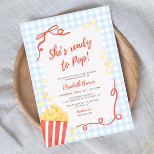 May include: Baby shower invitation with a blue gingham background and the text "She's ready to Pop!". The invitation includes details for Elisabeth Brown's baby shower, with a popcorn graphic in the corner.