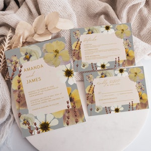 May include: A wedding invitation suite with a floral theme. The invitation features a gray background with pressed flowers in shades of yellow, white, and brown. The text reads "Amanda and James" in gold lettering. The RSVP card features a similar design with the text "Kindly RSVP by April 20th".