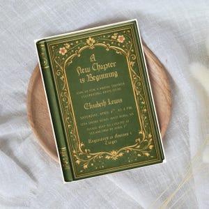 Può includere: Un biglietto d'invito verde progettato per assomigliare a un libro d'epoca. La copertina presenta decorazioni floreali dorate e il testo "A New Chapter is Beginning". Include il nome della sposa, la data, l'ora e le informazioni RSVP. È un invito a un addio al nubilato.