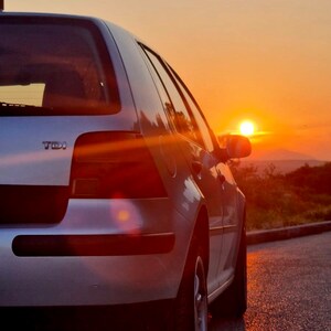 May include: A silver car parked on a paved road with the sun setting in the background. The car has a "TDI" emblem on the back.