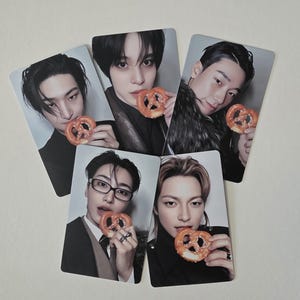 以下が含まれることがあります： それぞれプレッツェルを持っているさまざまな人々が写っている5枚の写真カード。カードは明るい背景です。カードの人々は黒髪で、黒い服を着ています。プレッツェルはゴールデンブラウンです。
