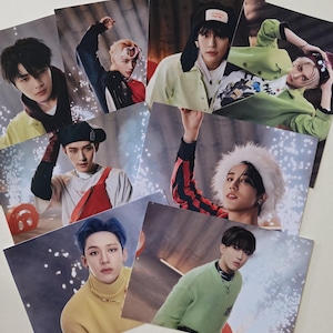 May include: A selection of glossy photo cards displaying different individuals in various poses and attire. The cards feature a range of colours, including red, green, yellow, and blue, with some wearing hats and jackets. The background has a blurred, textured appearance.