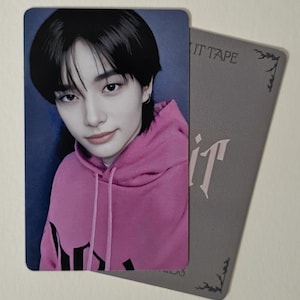 Peut inclure: Une carte photo rectangulaire représentant une personne portant un sweat à capuche rose. La personne a les cheveux noirs et regarde l'appareil photo. Une carte grise avec le texte "IT TAPE" et le mot "it" est à côté de la carte photo.