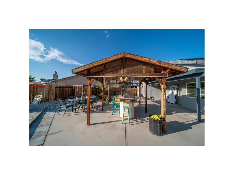 May include: A wooden pergola with a brown roof and a white mesh covering. The pergola is in a backyard with a patio set and a small pool.