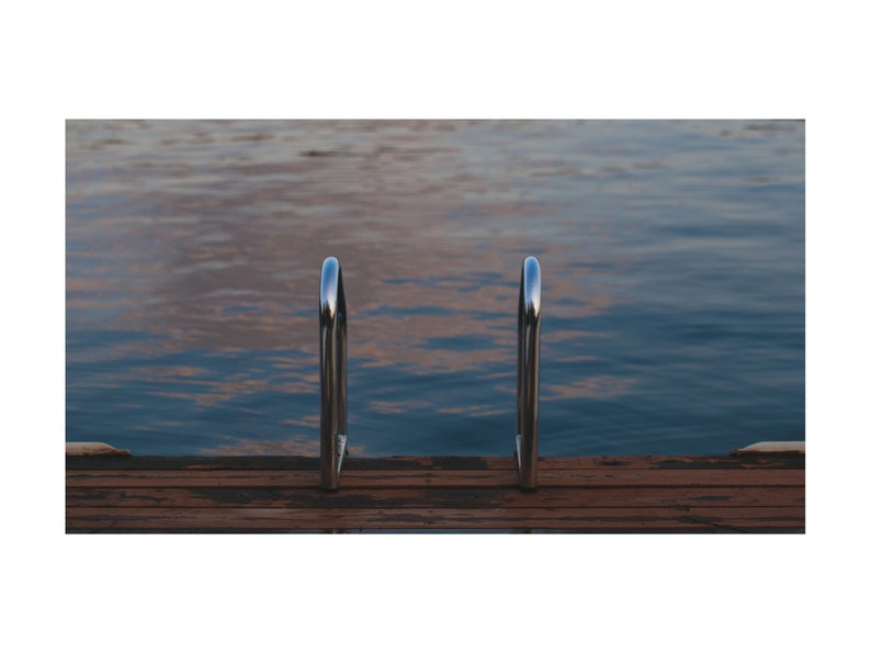 May include: A pair of silver metal handrails on a wooden dock over a body of water.