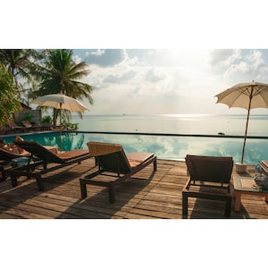 May include: A swimming pool with lounge chairs and umbrellas on a wooden deck overlooking the ocean. The pool is surrounded by lush tropical greenery.