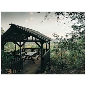 May include: A wooden gazebo with a picnic table and benches, overlooking a forest with a view of the horizon.