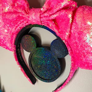 Può includere: Orecchie di Minnie Mouse rosa con paillettes, con un cerchietto nero e orecchie di Topolino con glitter iridescenti.