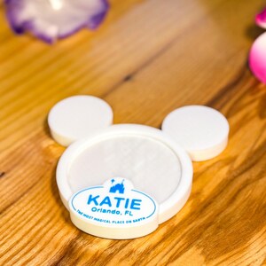 Könnte beinhalten: Weißer Teller in Mickey-Maus-Form mit einem blauen Aufkleber, auf dem "KATIE Orlando, FL The Most Magical Place on Earth" steht.