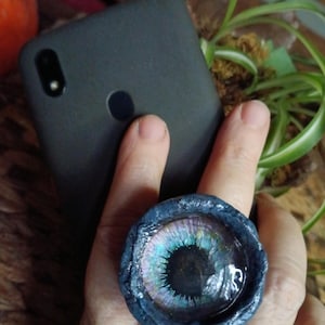 May include: A dark blue ring with a large, round, iridescent eye-shaped resin cabochon. The eye has a black pupil and a blue, green, and purple iris.