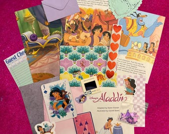 Peut inclure: Une collection d'éphémères en papier sur le thème d'Aladdin de Disney comprenant des pages de livre d'histoires, une carte à jouer avec Jasmine, un chèque d'invité, une enveloppe violette, un napperon en papier en forme de cœur et des confettis.
