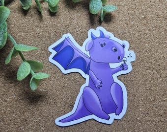 May include: A purple dragon sticker with blue wings and small horns. The dragon is blowing a dandelion puff. The sticker is on a brown surface with green leaves in the background. The dragon is a cartoon style.