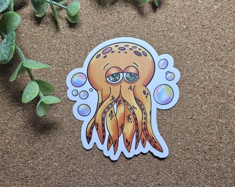 May include: A sticker featuring a cartoon octopus with an orange body and tentacles, and green eyes. The octopus has a sad expression and is surrounded by colorful bubbles. The sticker is on a brown surface.