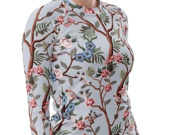May include: A long-sleeved shirt with a floral and bird pattern. The shirt features a light blue background with brown branches, pink and blue flowers, and small birds. The shirt is form-fitting and has a crew neck.