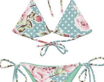 Könnte beinhalten: Zweiteiliger Bikini mit floralem Muster aus rosa Rosen und grünen Blättern auf hellblauem Hintergrund mit weißen Punkten. Das Bikinioberteil ist im Neckholder-Stil gehalten, die Hose zum Binden.
