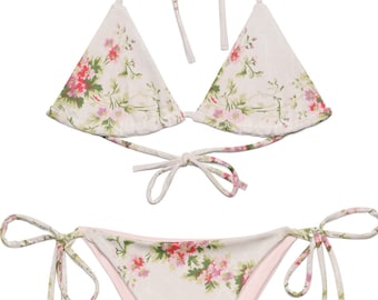 May include: A two-piece bikini set with a floral pattern. The bikini top is a triangle style with halter straps, and the bottoms are a tie-side design. The fabric features a cream background with pink and green floral accents.