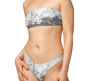 May include: A two-piece bikini set featuring a floral and striped pattern. The strapless top has a black and white striped band with a floral design above. The bottoms have a matching floral pattern.