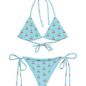 May include: A light blue bikini with a cherry print. The top is a triangle style with adjustable straps. The bottom is a cheeky style with ties on the sides.