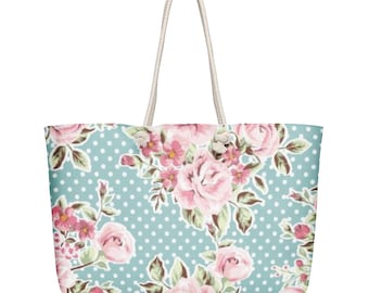 May include: A large tote bag with a floral pattern. The bag features a light blue background with white polka dots and a design of pink roses and smaller pink flowers. The handles are made of a cream-colored rope.