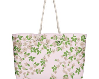 May include: A large tote bag with a light pink background and a floral pattern of white flowers and green leaves. The bag has white rope handles.