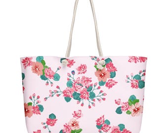 May include: A large tote bag with a light pink background and a repeating floral pattern in shades of pink, coral, and teal. The bag has white rope handles.
