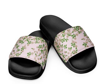 May include: Black slide sandals with a light pink floral pattern. The sandals have a black sole and a light pink strap with a repeating pattern of small white flowers and green leaves.