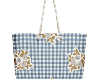 May include: A large tote bag with a blue and white gingham pattern and cream-colored rope handles. The bag features floral designs in shades of brown and cream. The bag is designed for carrying items.