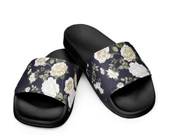 May include: Black slide sandals with a floral pattern. The sandals feature a dark navy blue strap adorned with white and yellow roses and green leaves. The soles are black.