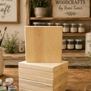 May include: A stack of six square, light-colored wooden blocks with a smooth, unfinished surface. The blocks are arranged vertically, with one block standing upright on top of the stack, showcasing the natural grain and texture of the light wood.