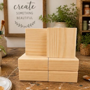 May include: A stack of six unfinished, light-colored wooden blocks. Two blocks are upright, and four are stacked below. A framed sign in the background reads "create something beautiful."