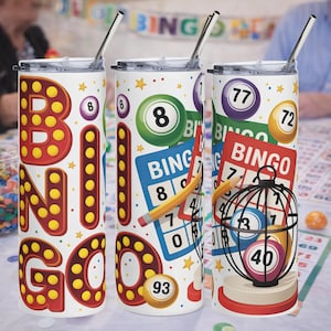 May include: Three white stainless steel tumblers with lids and straws, each featuring a different bingo-themed design. One tumbler has the word "BINGO" in large red and yellow letters. The other two have bingo balls, cards, and numbers.