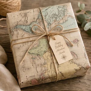 May include: A square gift box wrapped in vintage-style paper featuring a detailed world map in muted tones of beige, green, and blue. The package is tied with natural jute twine in a bow, holding a beige card tag printed with Happy Birthday Adventure Awaits.
