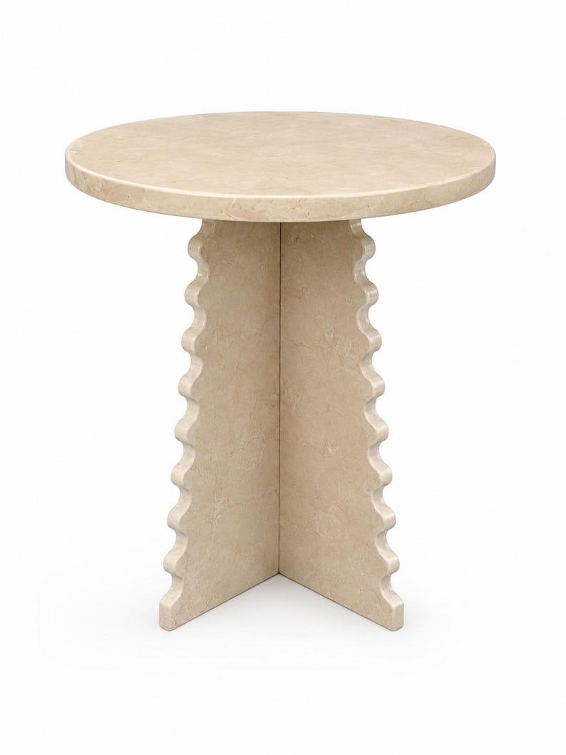 May include: A round side table crafted from beige stone with a smooth circular top. The base consists of two intersecting vertical panels featuring a distinct scalloped or wavy edge design along the outer sides, providing a stable foundation.