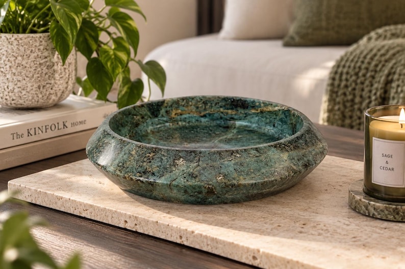 May include: A circular, shallow bowl crafted from polished green stone with natural dark veining and a smooth, glossy finish. The bowl features a wide, sloped rim and a deep center, showcasing the unique mineral patterns and textures of the stone.