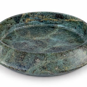 May include: A circular, shallow bowl crafted from dark green stone with natural veining and mottled patterns. The object features a wide, sloped rim and a smooth, polished surface, showcasing deep forest green tones with subtle black and grey inclusions.