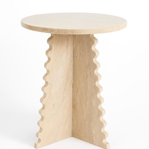 Pode incluir: Uma mesa lateral redonda bege com um design &uacute;nico. O tampo da mesa &eacute; liso e a base apresenta uma borda ondulada e recortada. A mesa &eacute; feita de um material de pedra de cor clara e tem aproximadamente 50 cm de di&acirc;metro.