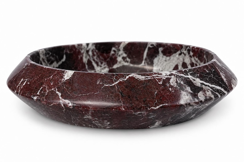 May include: A circular bowl crafted from deep burgundy marble with prominent white veining. The bowl features a wide, angled rim that slopes inward toward the center, showcasing a polished, smooth surface with natural stone patterns throughout.