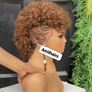 Peut inclure: Perruque bouclée marron avec des tresses complexes sur le côté, présentée sur une tête de mannequin. Le texte "Amiihairs" est visible. La perruque présente une ligne de cheveux naturelle et des boucles volumineuses.