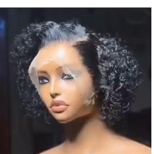 Può includere: Una parrucca nera riccia di capelli umani con un fronte in pizzo. La parrucca è acconciata con una riga laterale e i capelli sono ricci stretti.