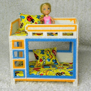May include: A white, blue, and orange bunk bed with a yellow and white patterned mattress and pillow. A doll is sitting on the top bunk.
